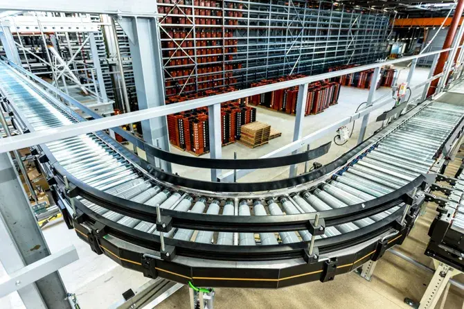 An overview of a modern production facility featuring a curved conveyor belt with storage racks filled with materials in the background