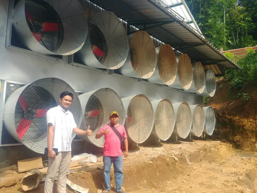 Twee mannen geven een duim omhoog voor een rij grote industriële ventilatoren buiten een boerderijgebouw