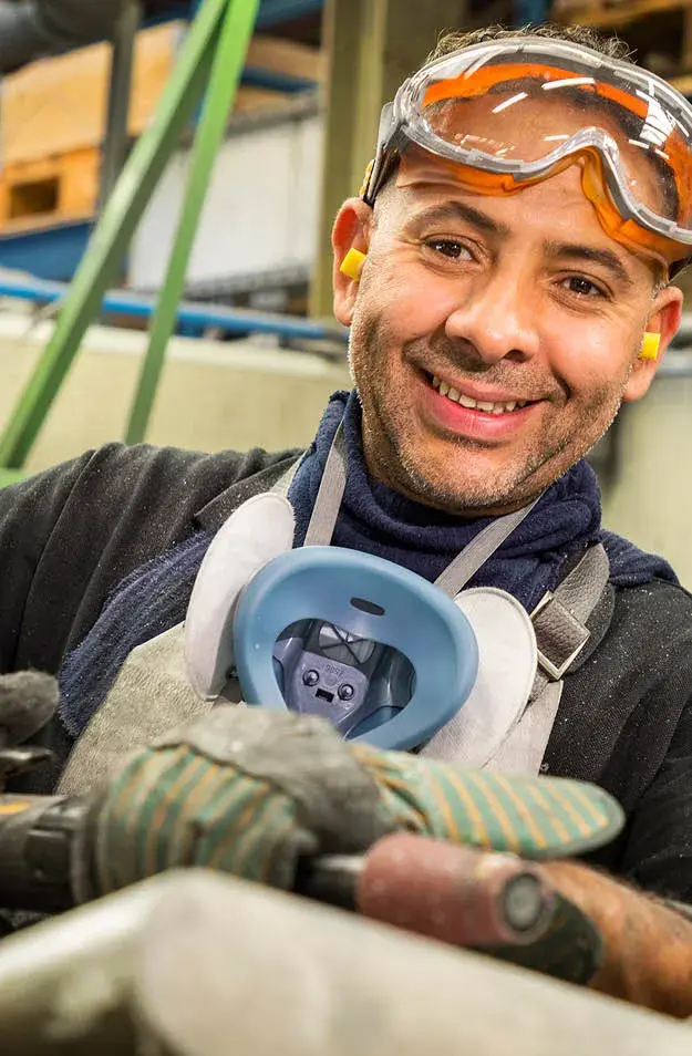 Glimlachende werknemer met veiligheidsbril en masker bezig met aluminium afwerking