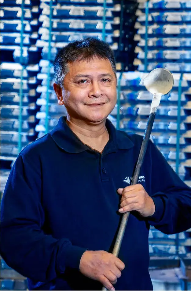 Employee holding casting tool in front of stacked materials in a gravity die casting facility