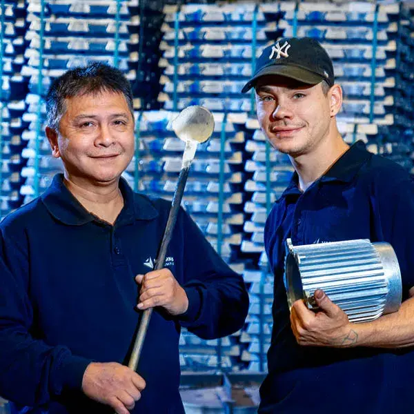 Two employees working in gravity die casting holding tools and metal components