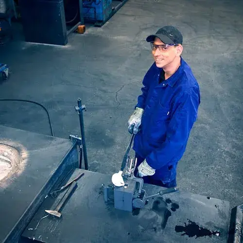 Werknemer werkt aan zwaartekrachtgieten op een werkstation, draagt beschermende handschoenen en bril