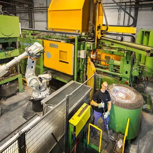 Worker operating machinery in a high pressure die casting facility with robot arm