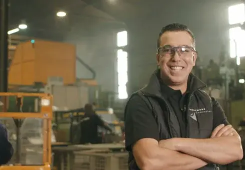 Travailleur souriant avec des lunettes de sécurité devant un équipement de fonderie sous pression