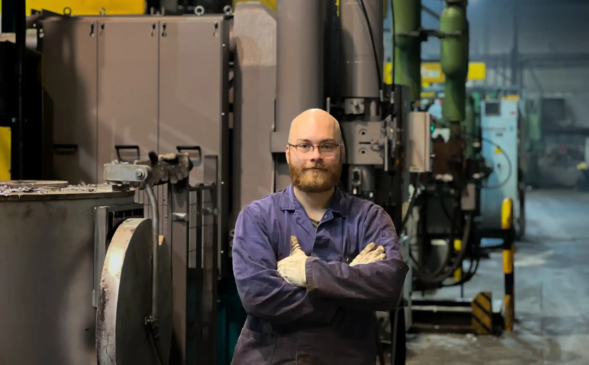 Maintenance technician with arms crossed in front of machinery in a workshop