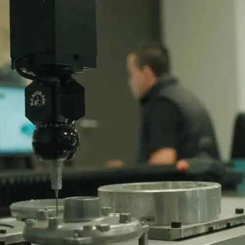 Close-up of a quality assurance machine inspecting metal components with a technician in the background