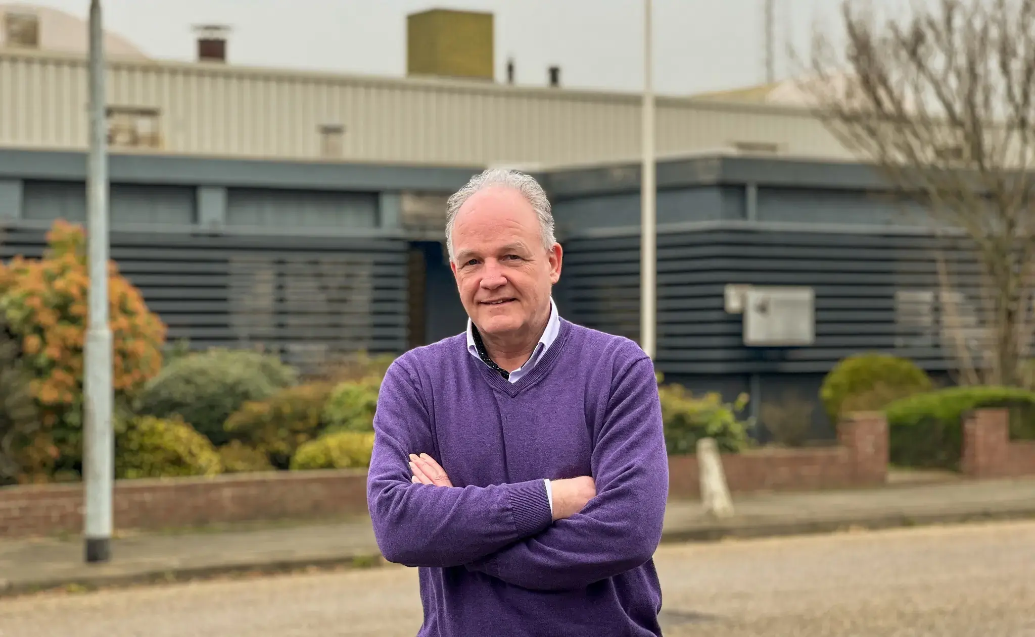 Verkoopmedewerker staat buiten met gekruiste armen voor een industrieel gebouw