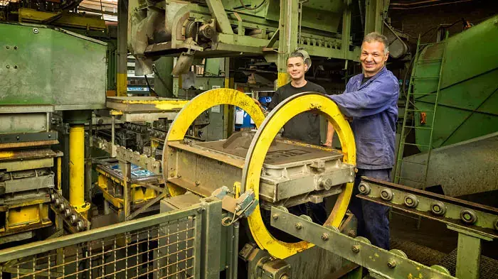 Employees working with sand casting machinery in a factory
