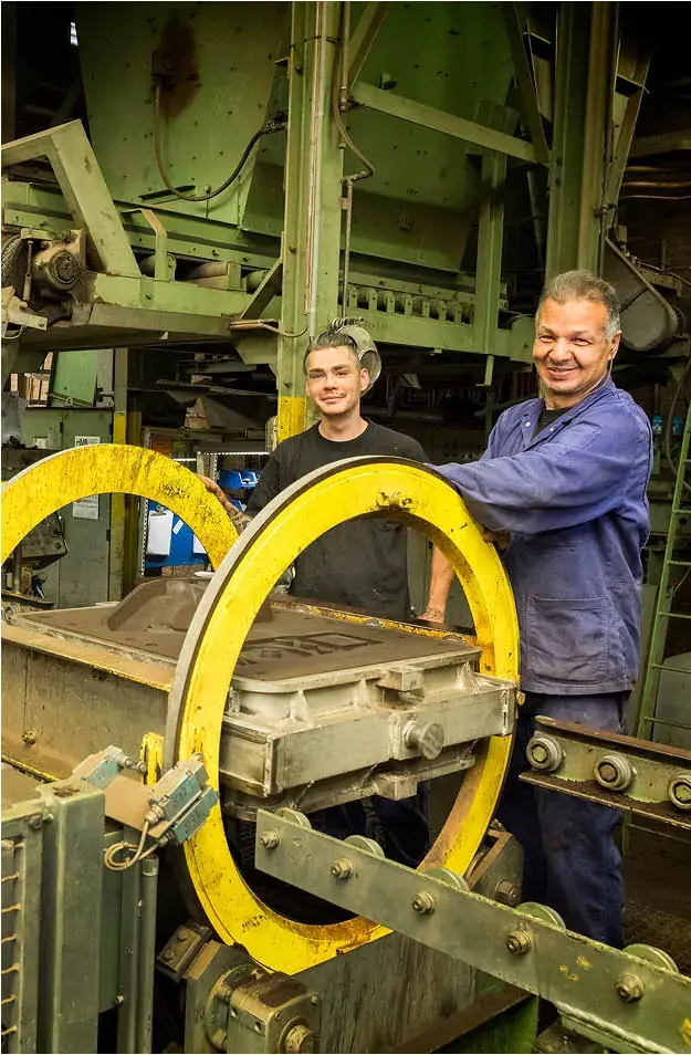 Medewerkers werken met zandgietmachine en glimlachen naar de camera in een fabriek