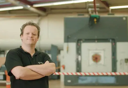 Employee standing with arms crossed in front of testing equipment in research and development facility