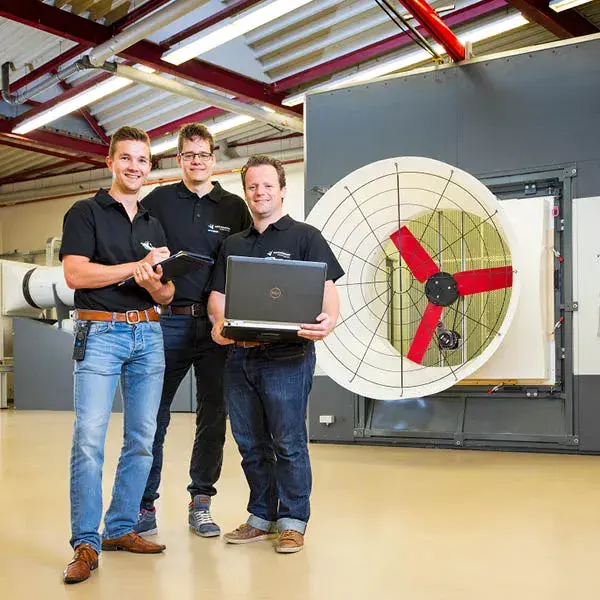 Three employees standing in front of a large fan in research and development facility