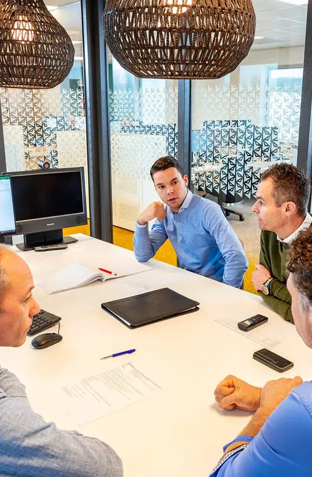 Equipo de ventas discutiendo estrategia en oficina moderna con portátil y documentos sobre la mesa