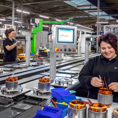 Zwei Frauen arbeiten in einer Fabrik und wickeln Spulen an Maschinen für Lüftungsanlagen