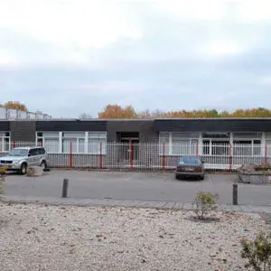 Vista exterior de un edificio moderno con una entrada vallada con coches aparcados y una zona ajardinada que marca la adquisición de EMI Indolec en 2006