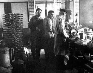 Three people working in a factory with stacked fan blades in the background