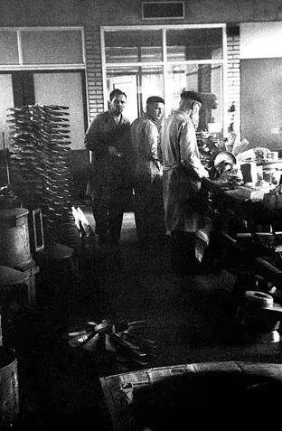 Three workers in a factory setting engage in tasks surrounded by machinery and materials showcasing an industrial environment