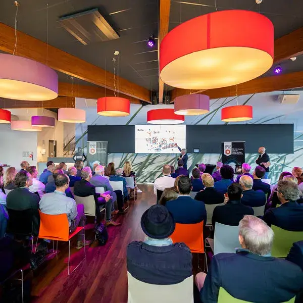 Een presentatie in een modern auditorium met een publiek dat naar een spreker kijkt