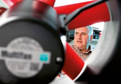 Retrato de un hombre que mira a través de un ventilador industrial, centrándose en la etiqueta del ventilador. 